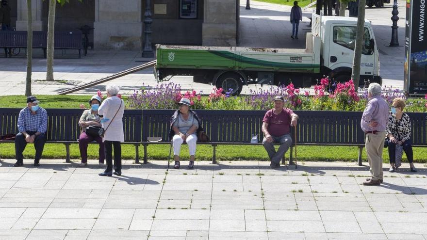 Personas mayores con mascarilla, sentadas en un banco manteniendo la distancia social de seguridad.