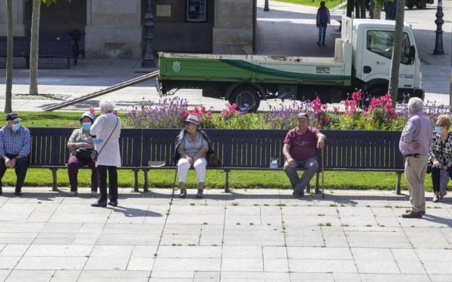 Personas mayores con mascarilla, sentadas en un banco manteniendo la distancia social de seguridad.