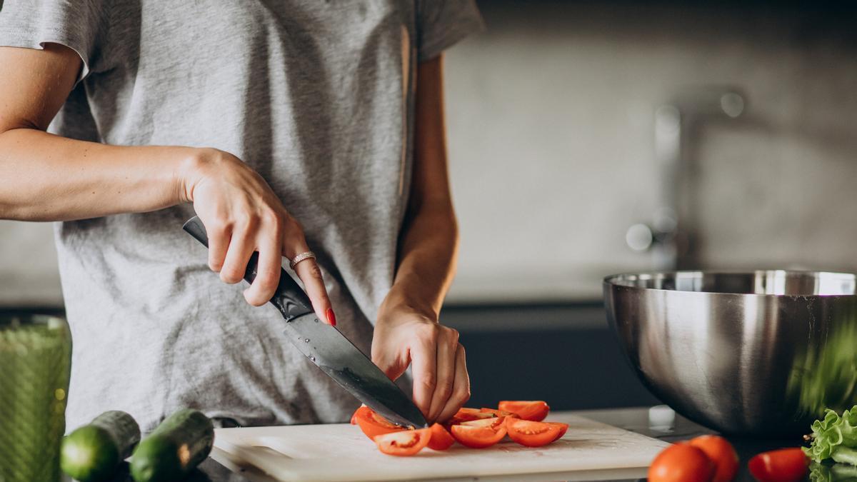 Mujer corta un tomate para preparar una receta en casa