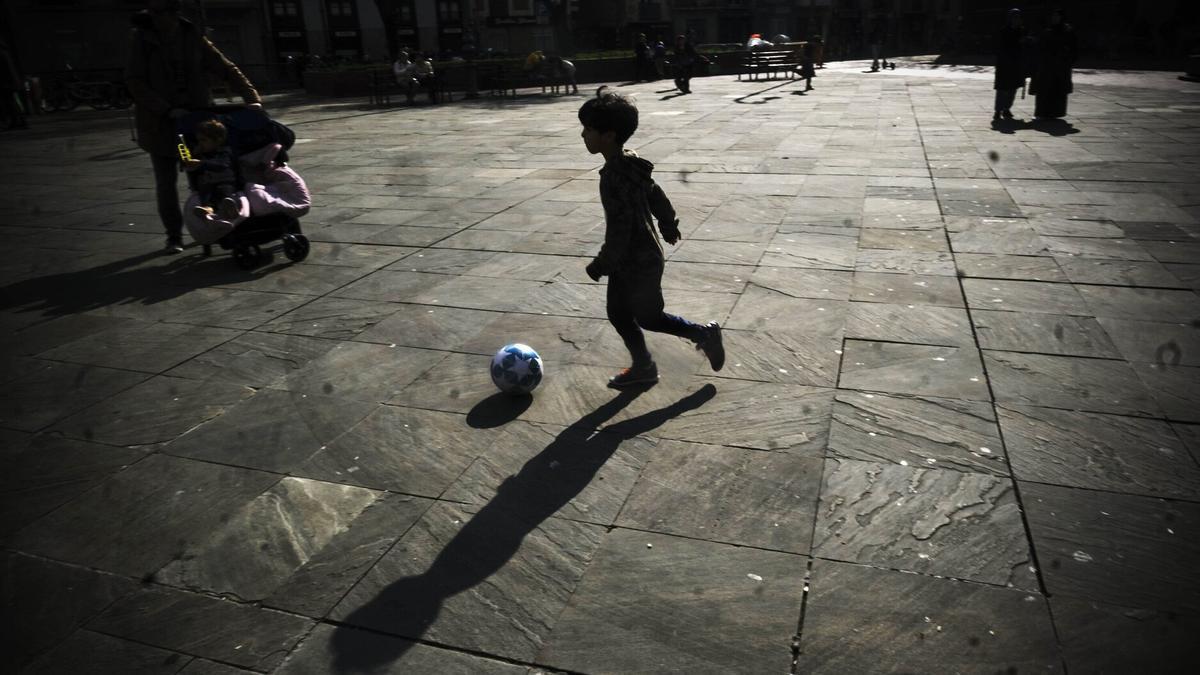 Un menor jugando con el balón en una plaza.