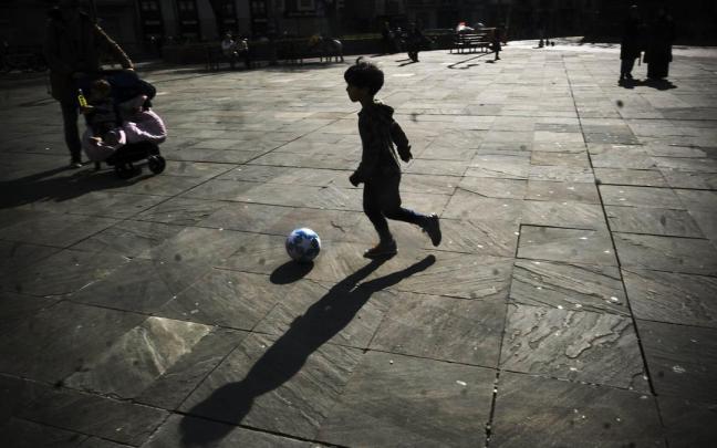 Un menor jugando con el balón en una plaza.