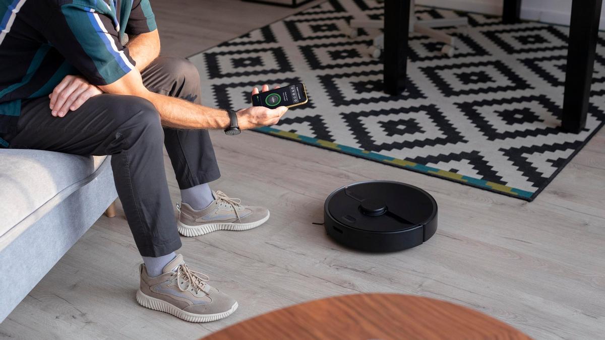 Hombre controlando su aspiradora robot desde el móvil.