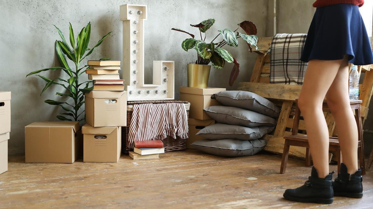 Rincón de una habitación lleno de cajas, libros y cojines por el suelo.