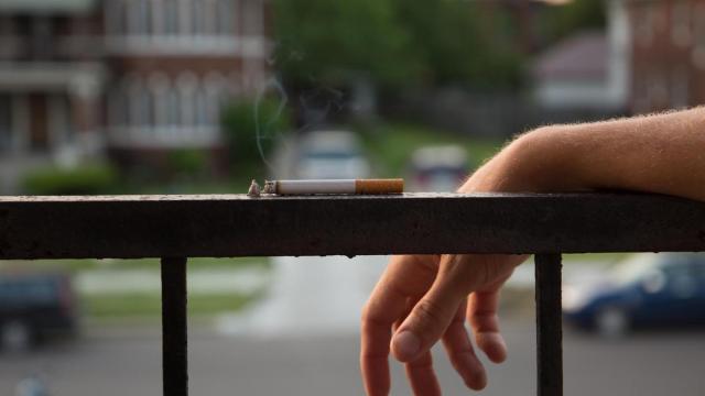 Un hombre coloca un cigarrillo encendido sobre la barandilla de un balcón.