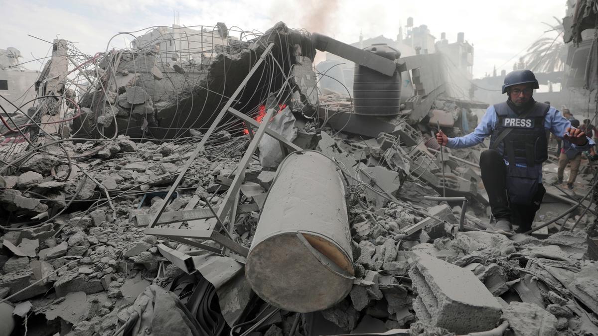 Un periodista intenta caminar ente los escombros de un edificio destruido por los bombardeos israelíes.