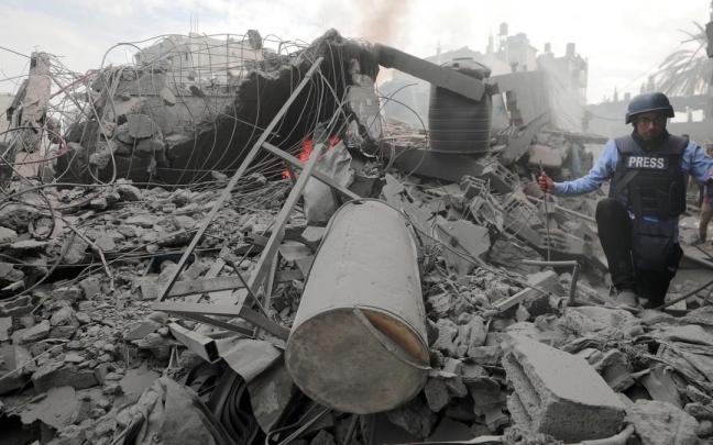 Un periodista intenta caminar ente los escombros de un edificio destruido por los bombardeos israelíes.