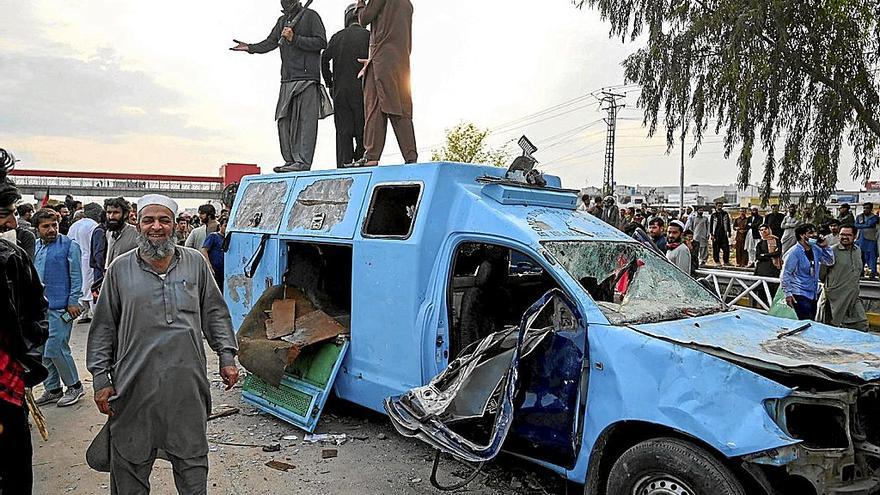 Seguidores del ex primer ministro Imran Khan posan junto a un vehículo policial destruido.