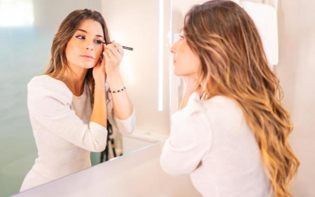 Una mujer se maquilla delante de un espejo.