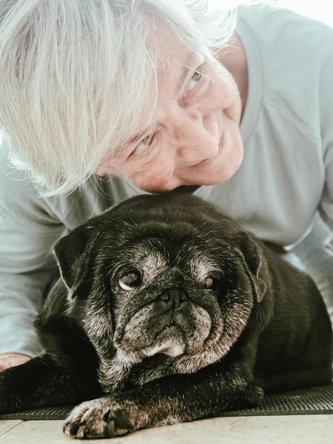 Una mujer hace mimos y abraza a su pug sénior.