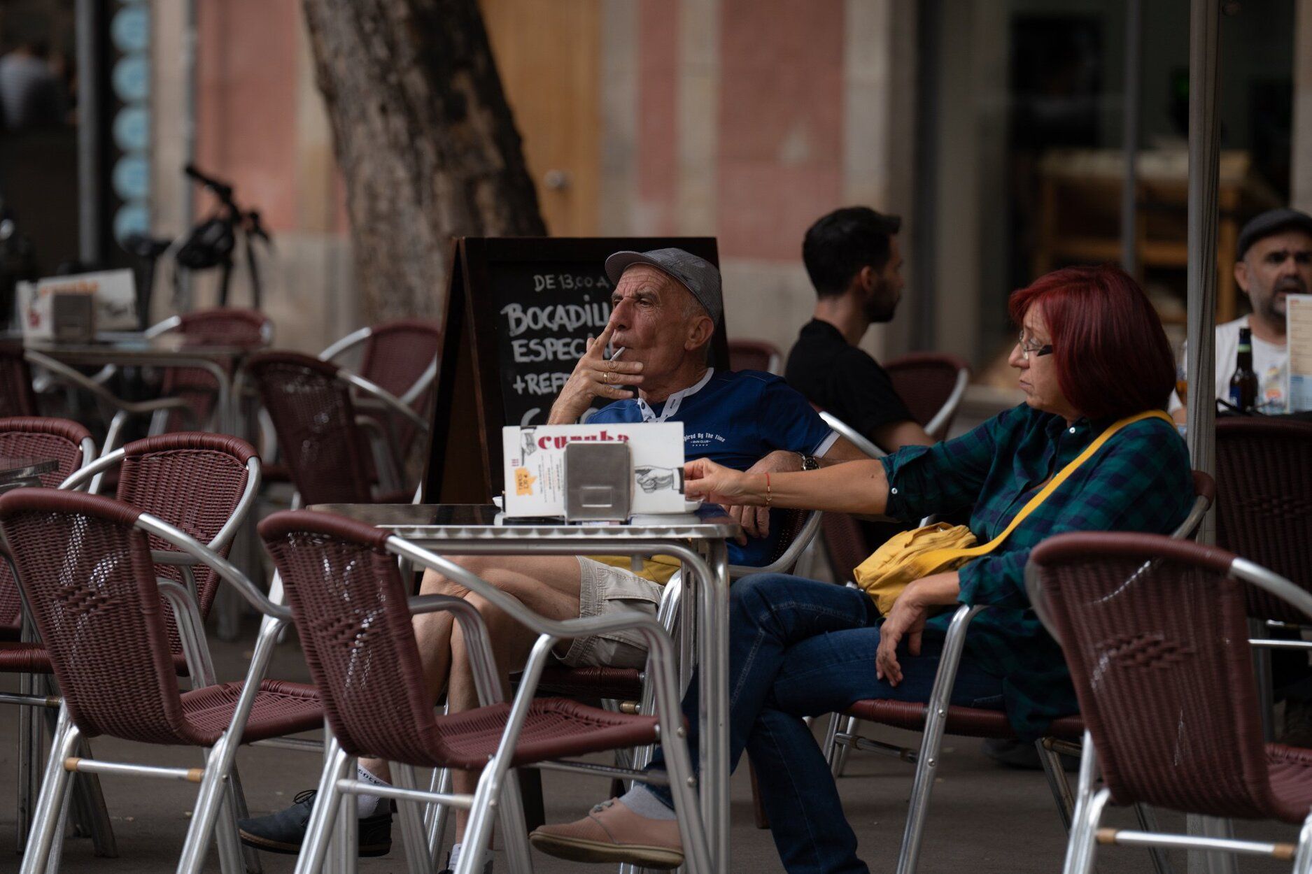 Una persona mayor fuma tranquilamente un cigarrillo en una terraza.