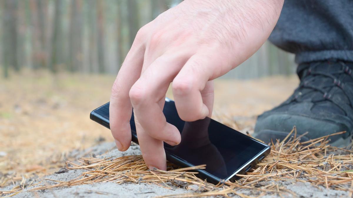 Un hombre recoge un móvil perdido en el bosque.