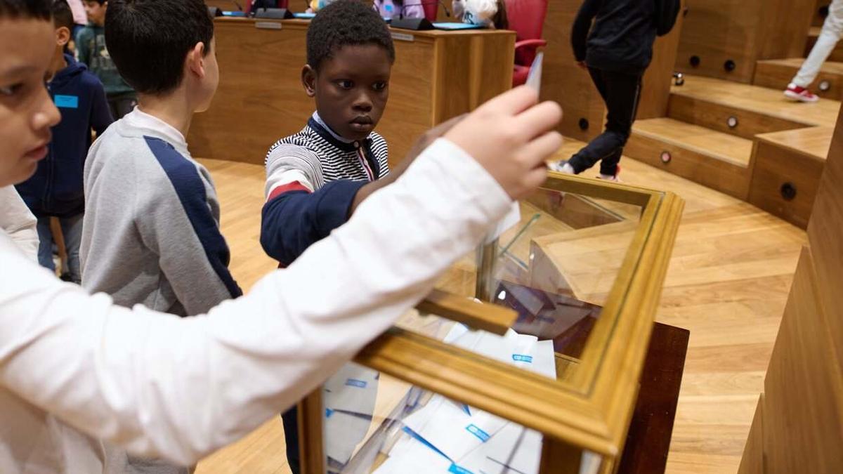 Varios escolares depositan su voto en una urna.