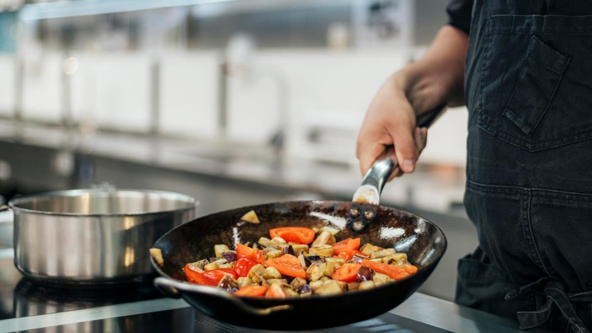 Un hombre con un delantal cocina verduras en una sartén de hierro.