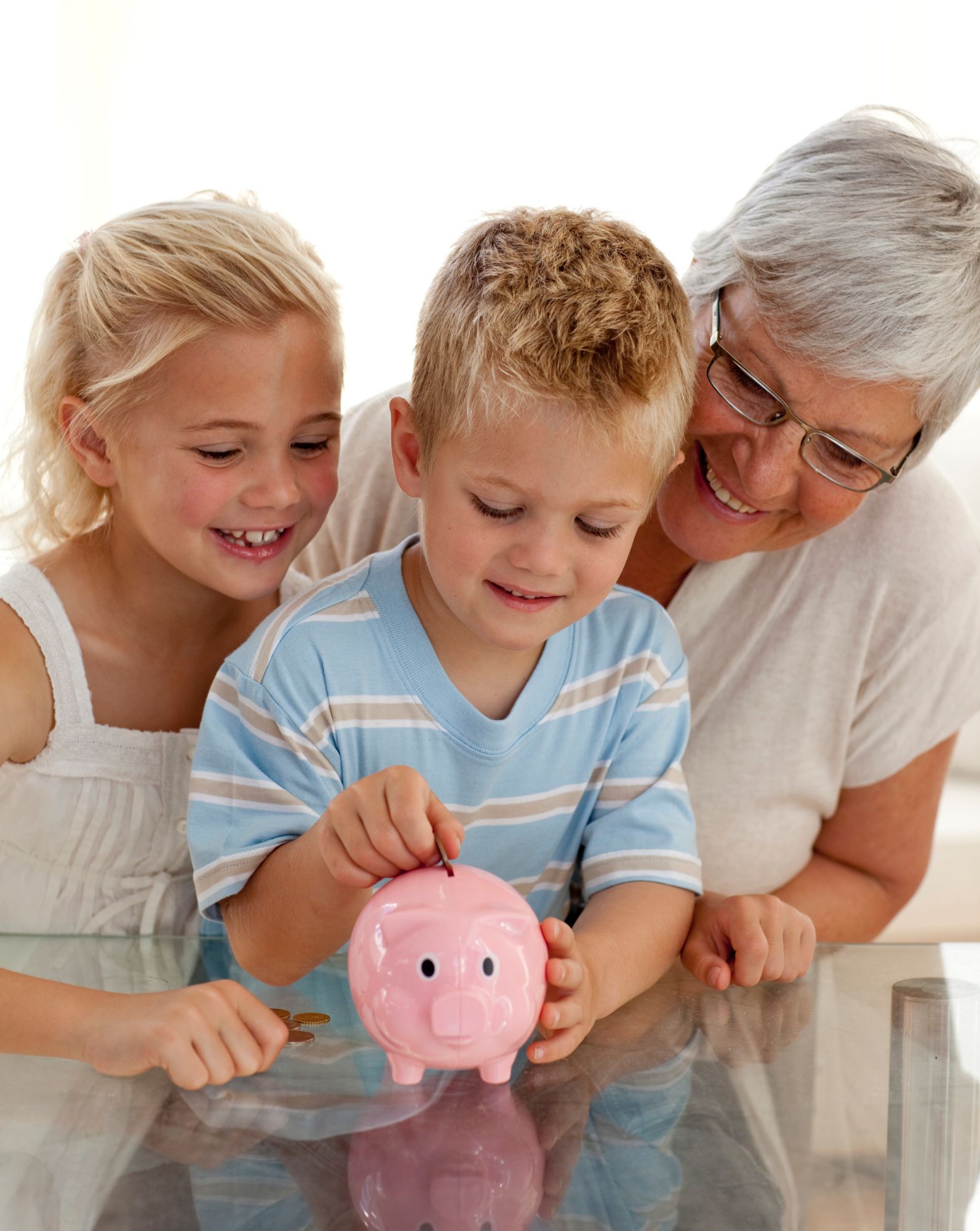 Un niño mete una moneda a la hucha en presencia de su hermana y de su abuela.