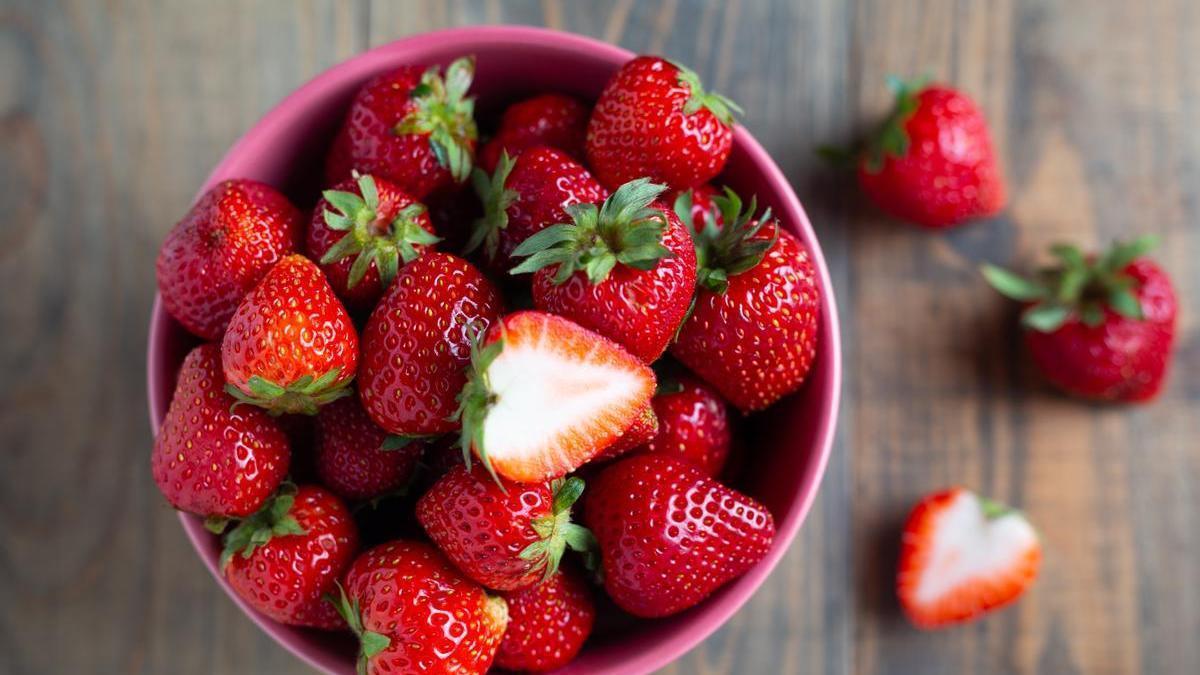 Fresas en un recipiente rosa sobre una mesa de madera.