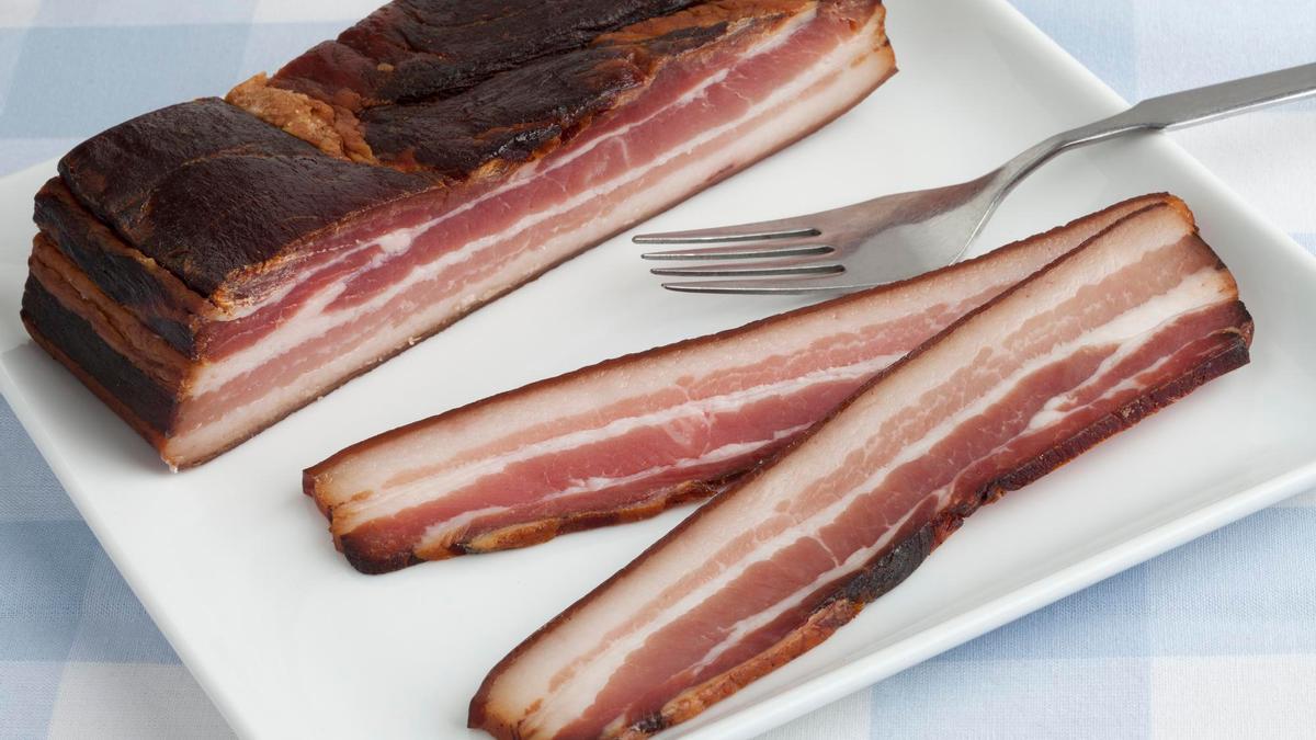 Una pieza de panceta curada y dos lonchas listas para cocinar.