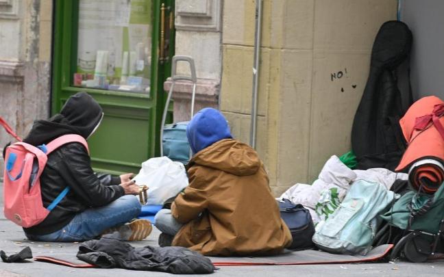 Dos personas sin hogar sentadas en la calle.