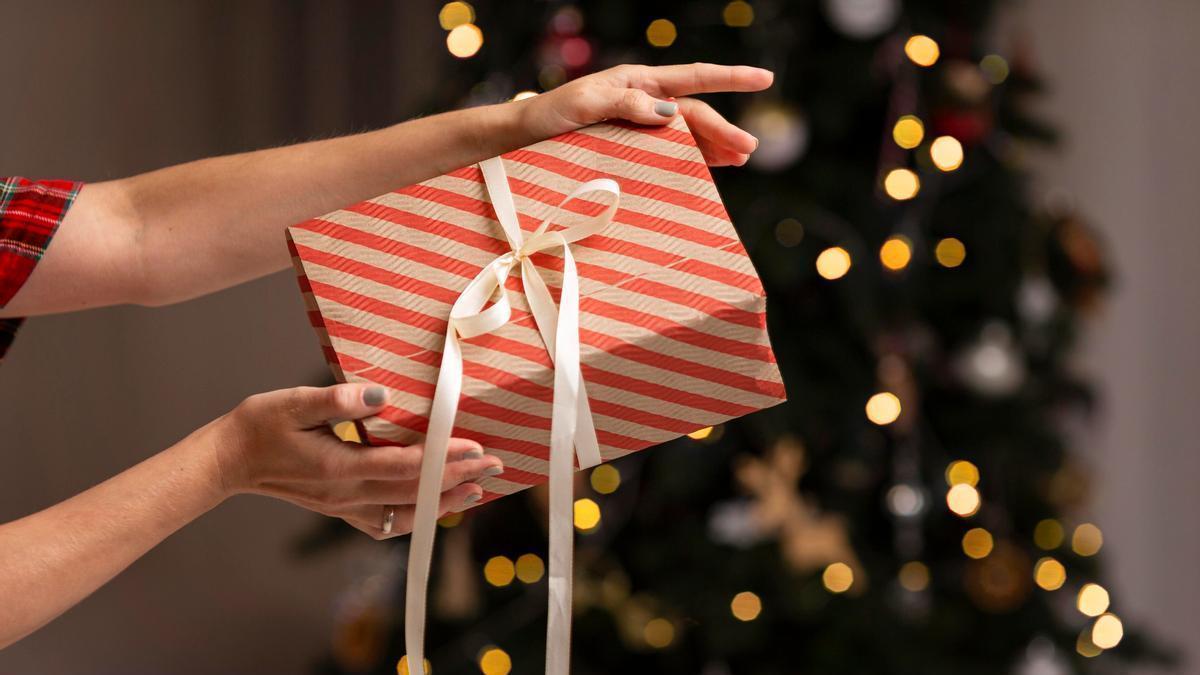 Manos de una chica sujetando un regalo con el árbol de Navidad de fondo