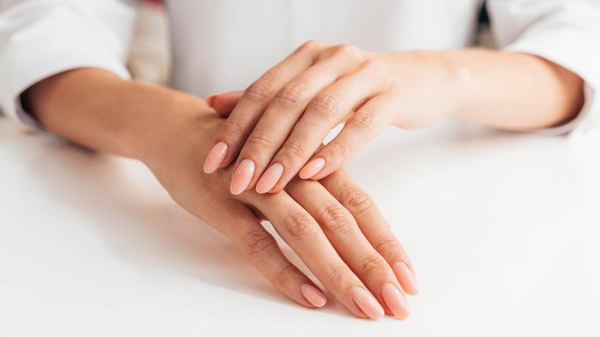 Una mujer luce una bonita manicura en un tono rosa claro.