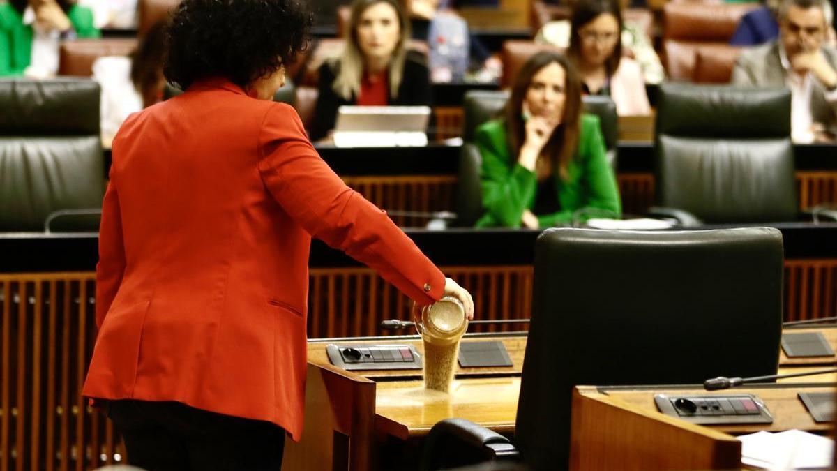 La diputada del Grupo Mixto Maribel Mora derrama arena en el escaño del presidente de la Junta, Juanma Moreno, durante el pleno del Parlamento andaluz.