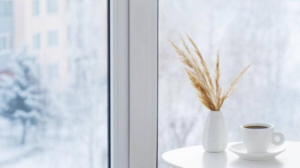 Taza de café y jarrón junto a una ventana de casa en invierno