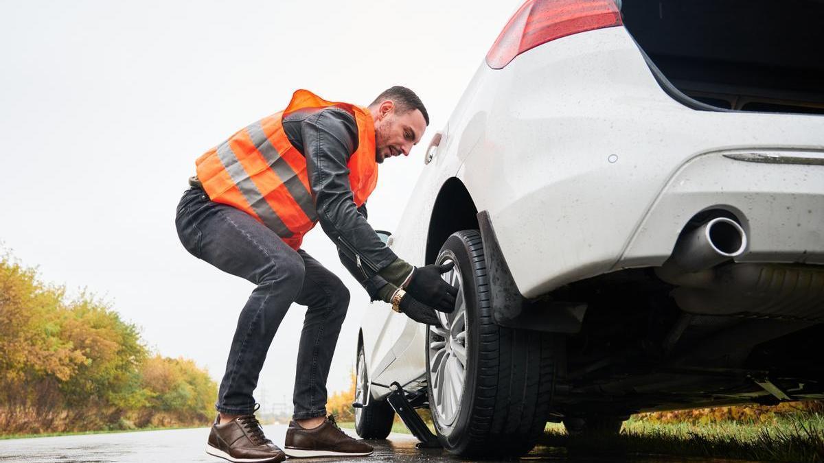 Hombre cambia un neumático en la carretera debido a un pinchazo.