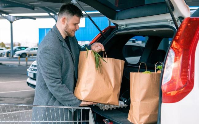 Un hombre coloca las bolsas en el maletero del coche.