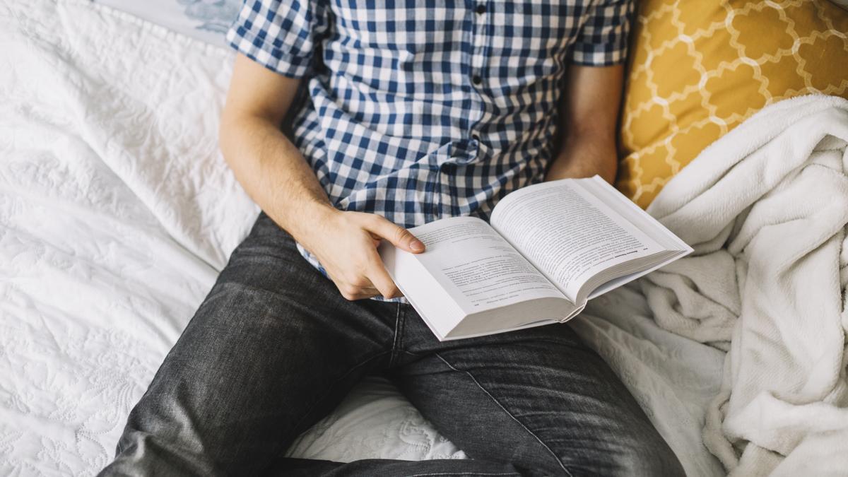 Un hombre, leyendo un libro en la cama.