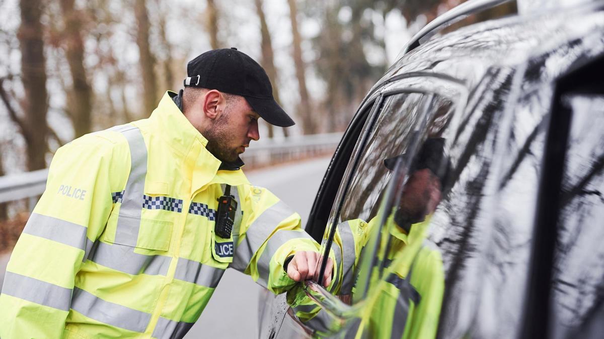 Agente de tráfico parando a un coche de color oscuro.