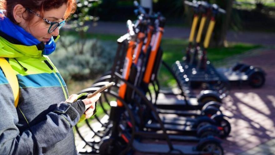 Una chica utiliza su teléfono móvil para alquilar un patinete eléctrico.