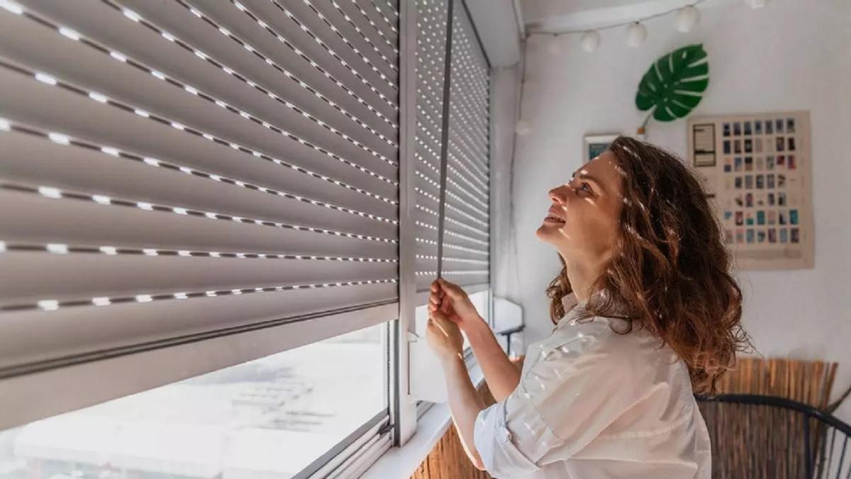 Una mujer sube la persiana de su habitación