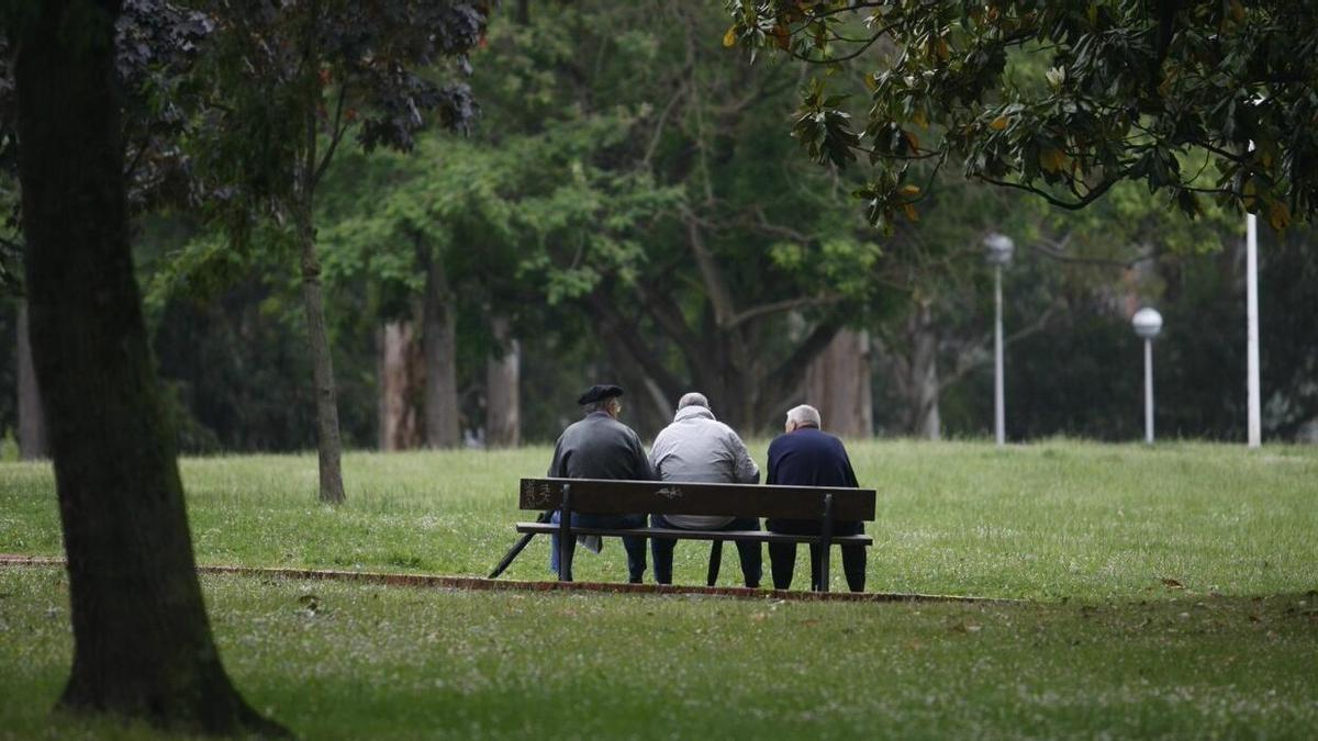 Tres ancianos sentados en un banco en un parque.