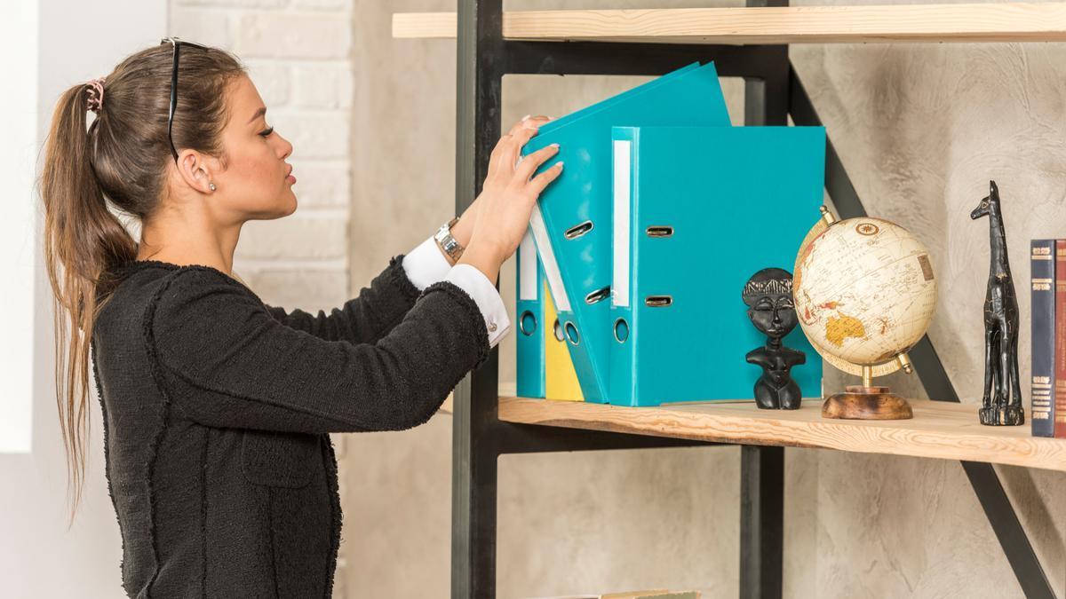 Una mujer coge un archivador de una estantería.