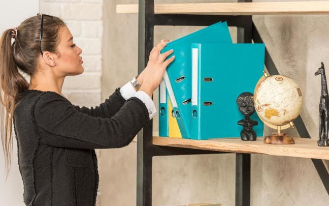 Una mujer coge un archivador de una estantería.