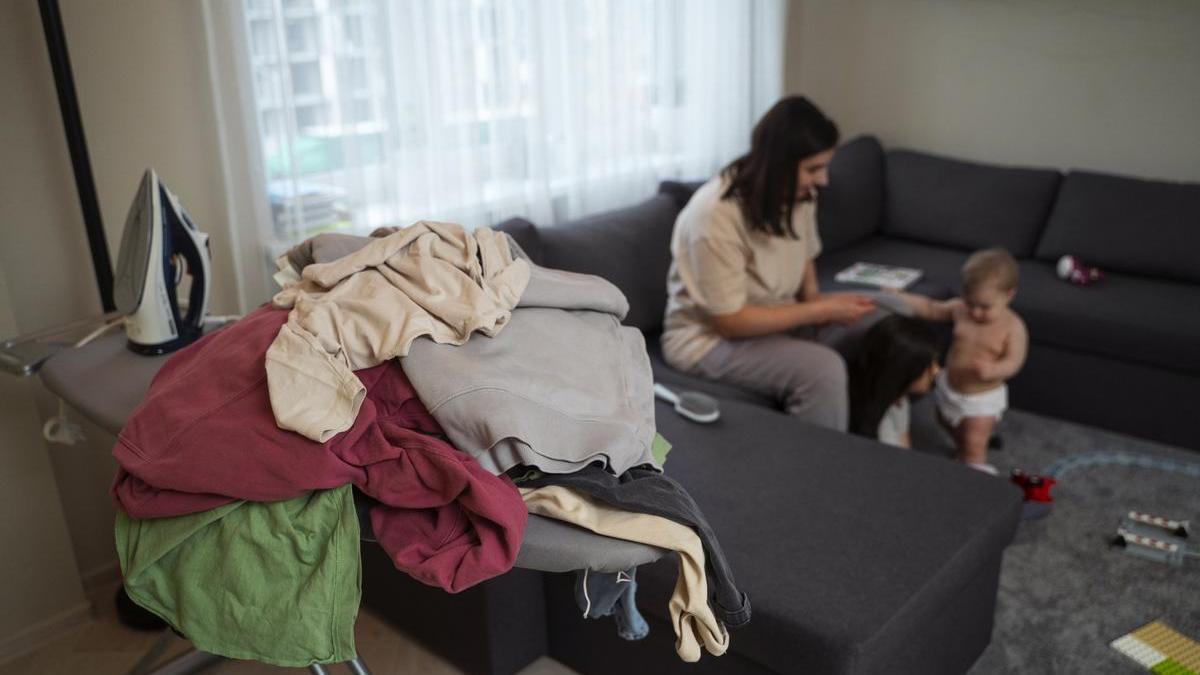 Madre y su hijo en el salón con un montón de ropa acumulada para planchar.