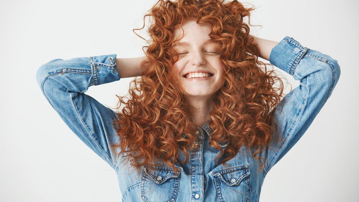 Chica sonriente tocando su pelo rizado.