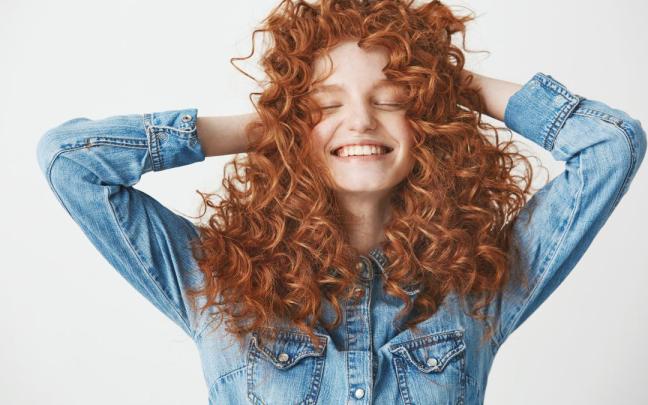 Chica sonriente tocando su pelo rizado.