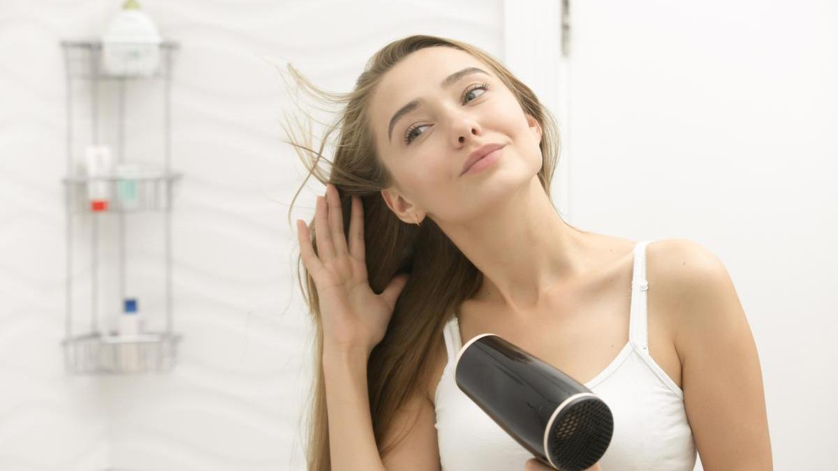 Mujer se seca el pelo frente al espejo para quitar el exceso de humedad antes de acostarse.