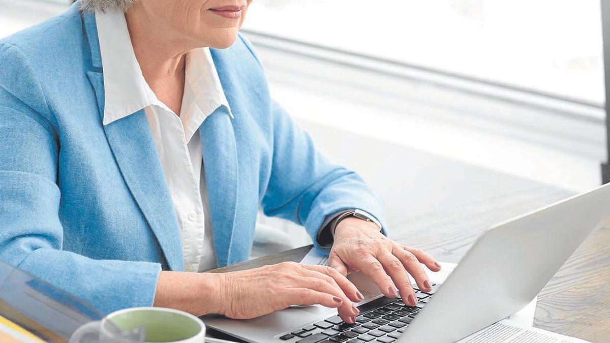 Una mujer jubilada realiza gestiones administrativas con un ordenador portátil.