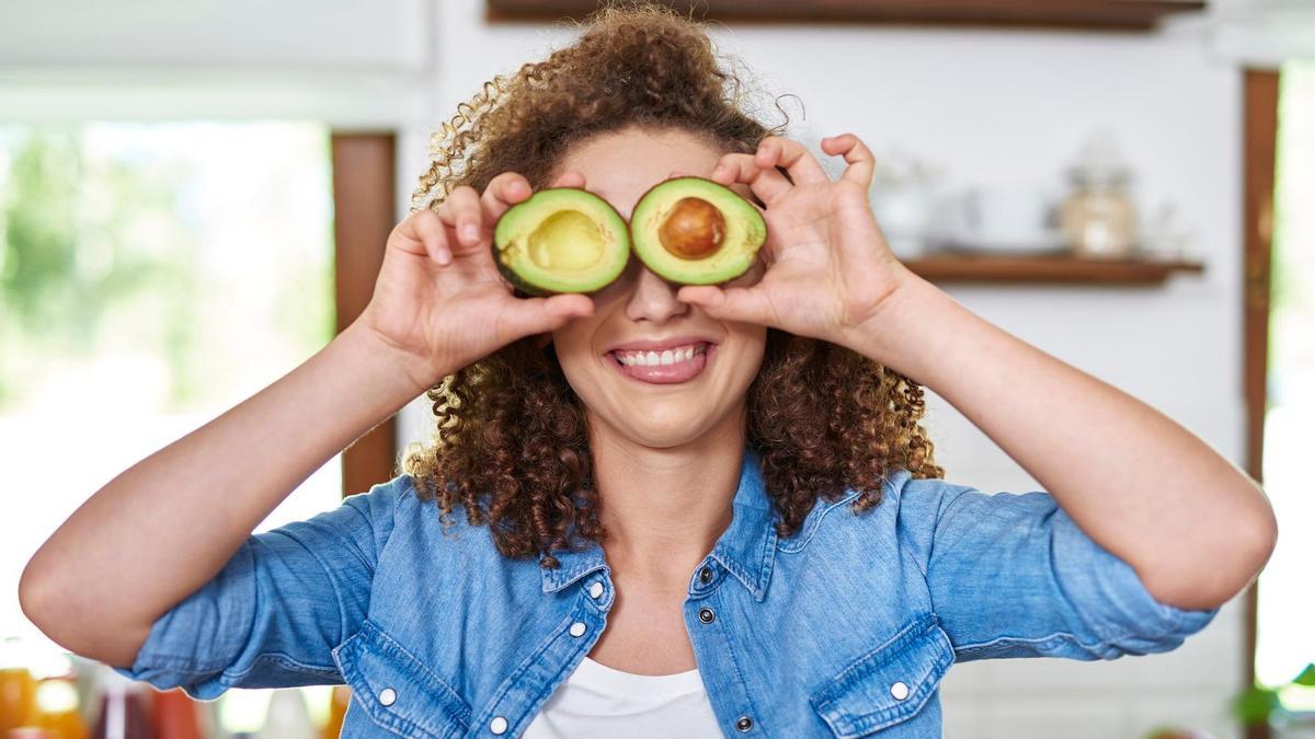 Una mujer se tapa los ojos con un aguacate abierto. Una mujer se tapa los ojos con un aguacate abierto.