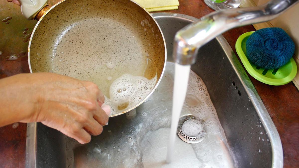 Una persona lava una sartén en la fregadera después de cocinar.