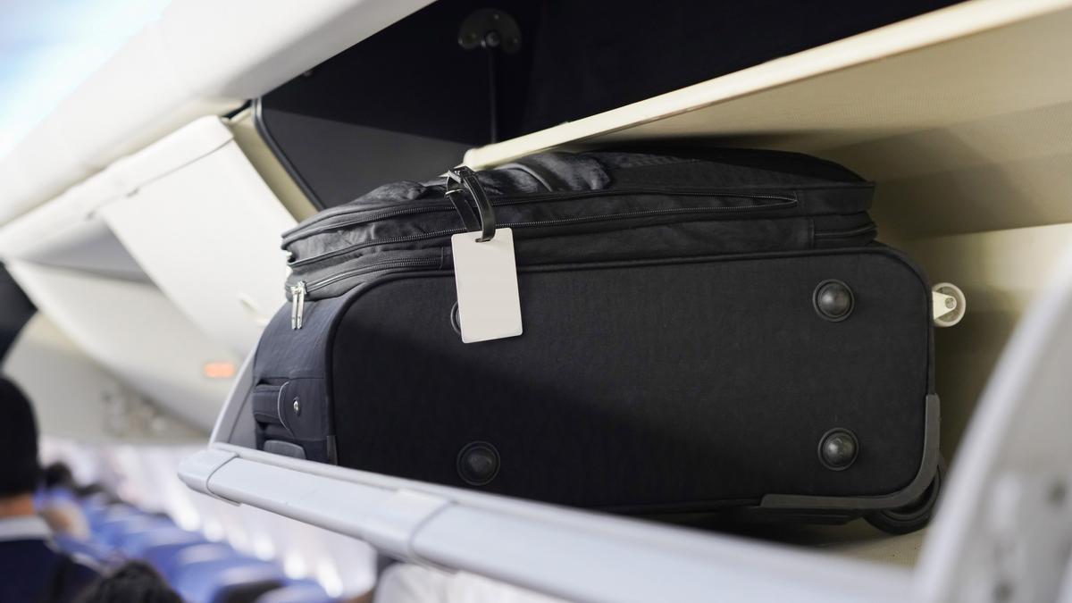Una maleta de mano, en el estante de la cabina de un avión.