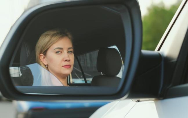 Una mujer reflejada en el espejo retrovisor lateral izquierdo.