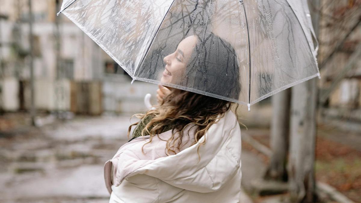 Chica bajo la lluvia con un paraguas transparente y una chaqueta acolchada