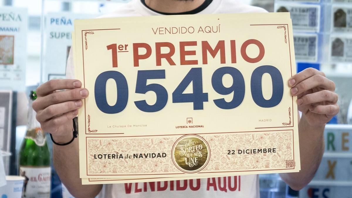 Un empleado de una de las la administraciones que vendieron el Gordo de 2022, el 05490, con un cartel con el número.
