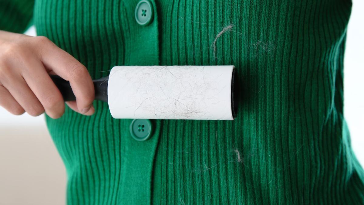 Una mujer se quita las pelusas de la chaqueta con un rodillo adhesivo.