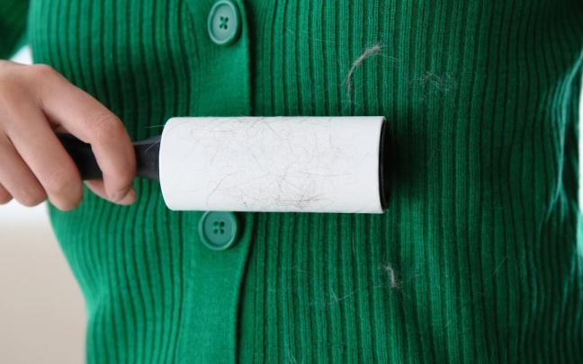 Una mujer se quita las pelusas de la chaqueta con un rodillo adhesivo.