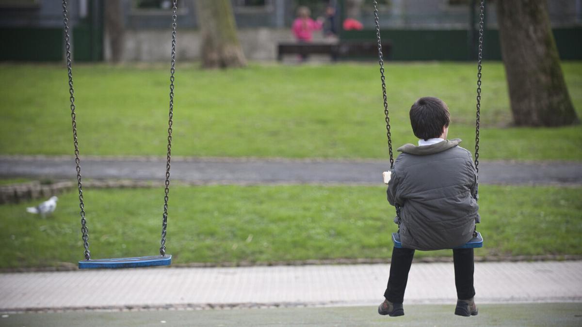 Un menor tomando su merienda a solas en el columpio de un parque.