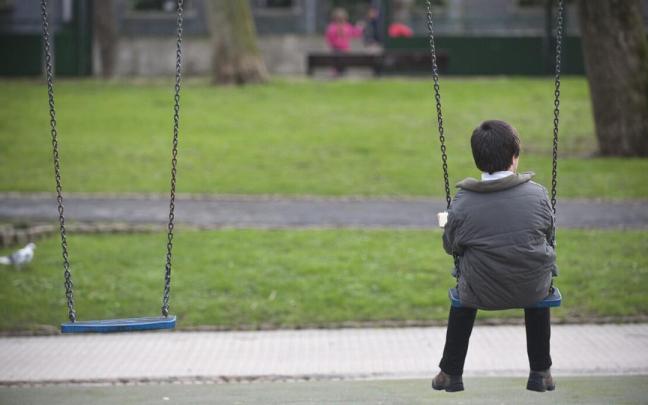 Un menor tomando su merienda a solas en el columpio de un parque. Un menor tomando su merienda a solas en el columpio de un parque.