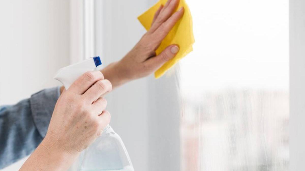 Manos limpiando los cristales con un producto de limpieza en spray y un paño de microfibra